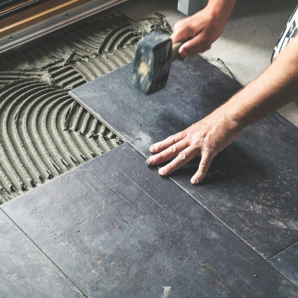 closeup of flooring expert installing new black roof tiles on a floor using a rubber mallet