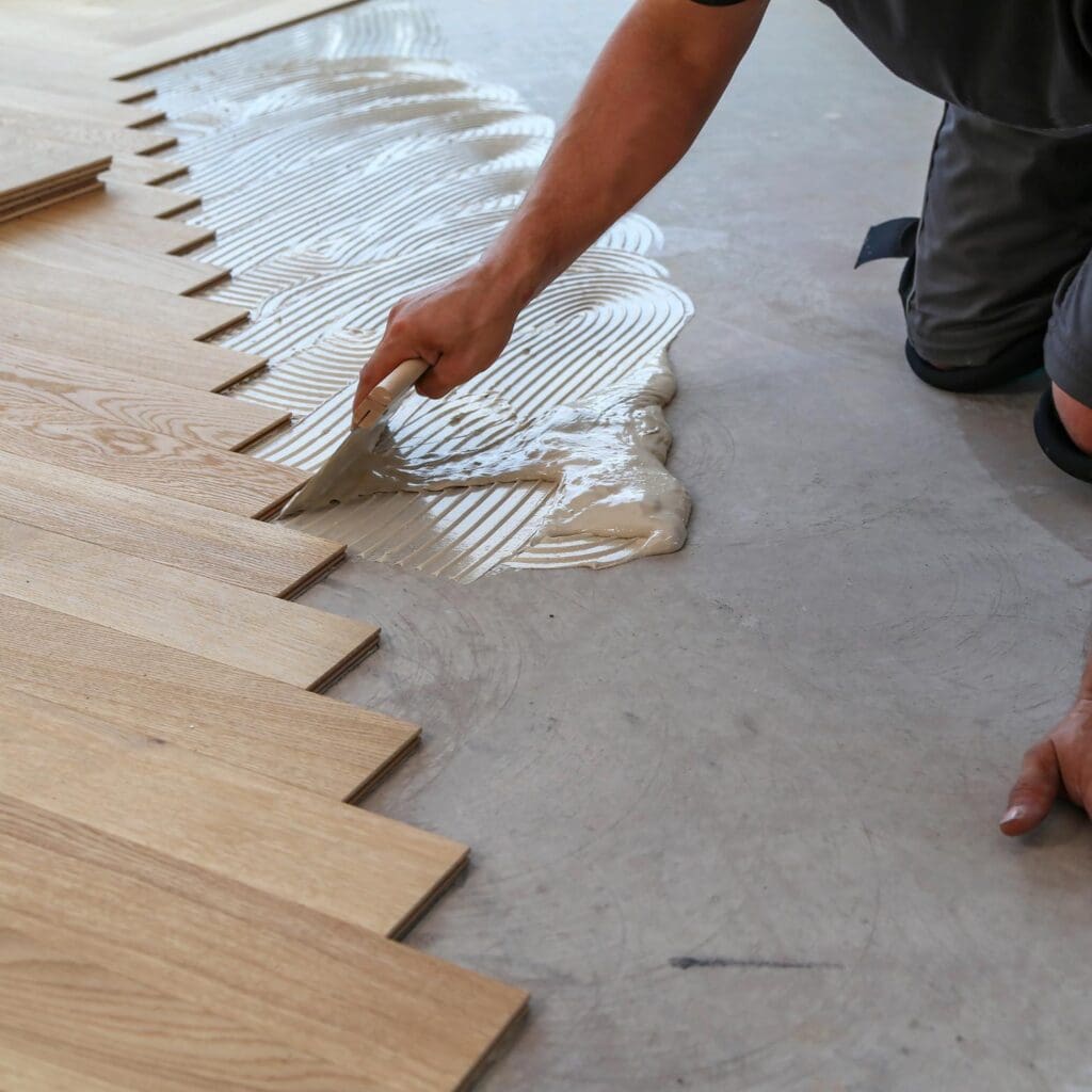 floor expert pouring adhesive tile glue so as to install wooden tiles